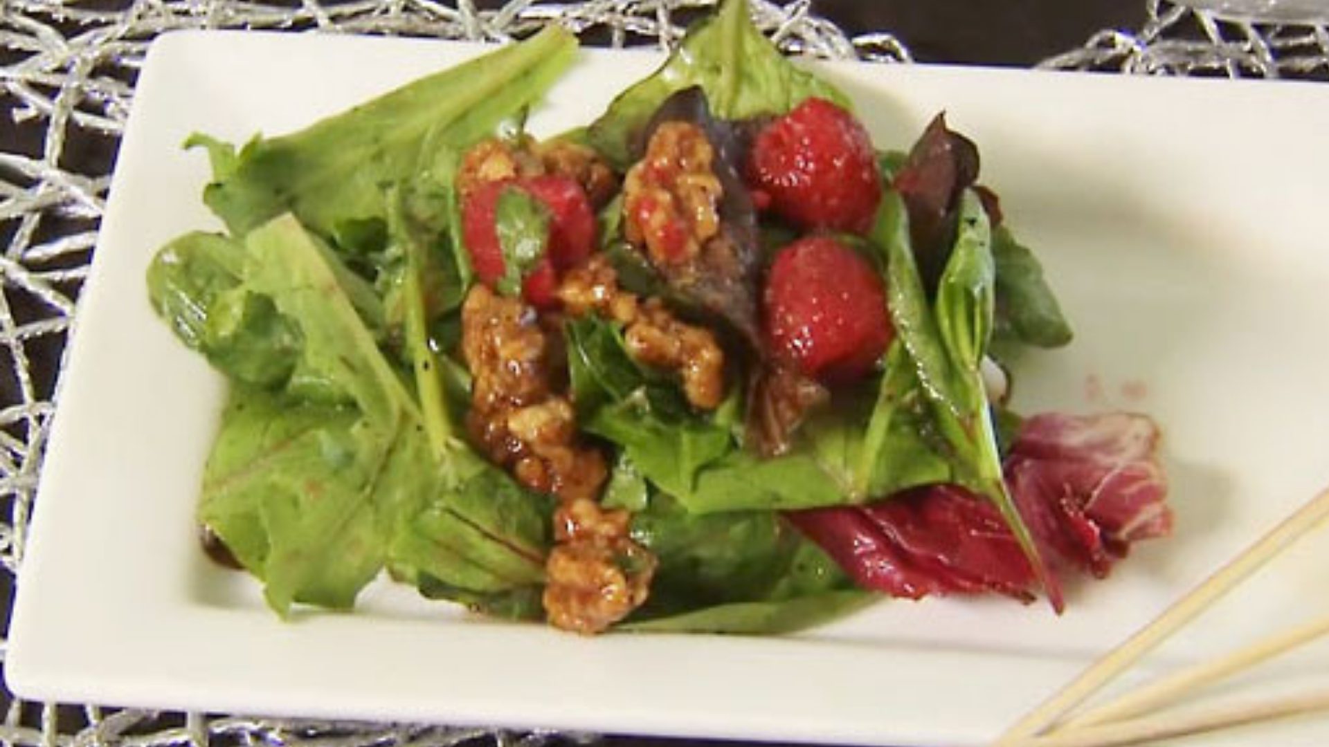 A salad with lettuce, raspberries, and caramel coated walnuts on top of a plate. 