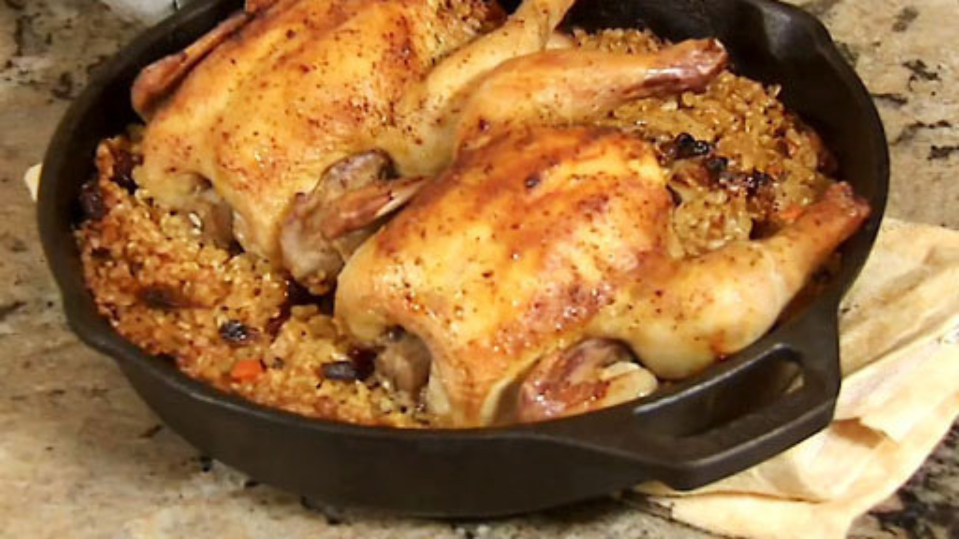 Two small roasted Cornish hens, filled with rice pilaf and served in a small cast iron skillet.