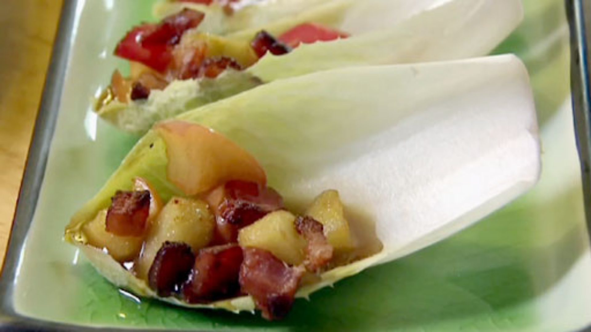 A plate with endive leaves that are filled with caramelized apples and bacon.