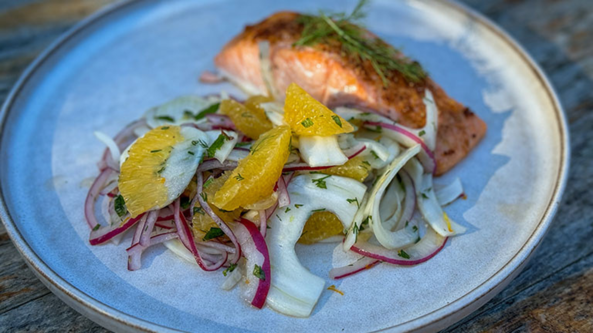 An orange and fennel salad plated alongside roasted salmon and garnished with herbs.