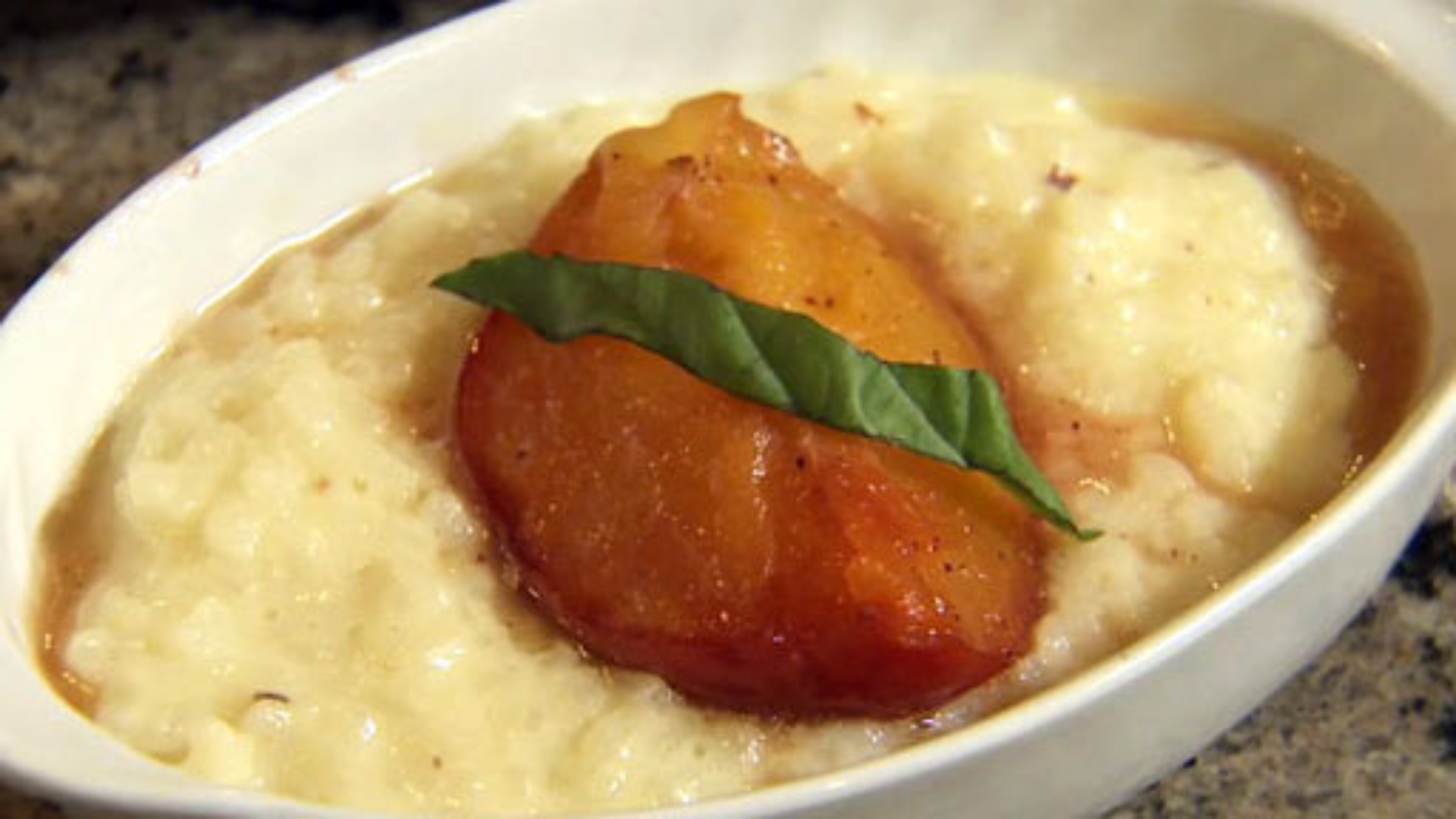 A ceramic bowl filled with creamy rice pudding, which is topped with a caramelized peach and basil. 