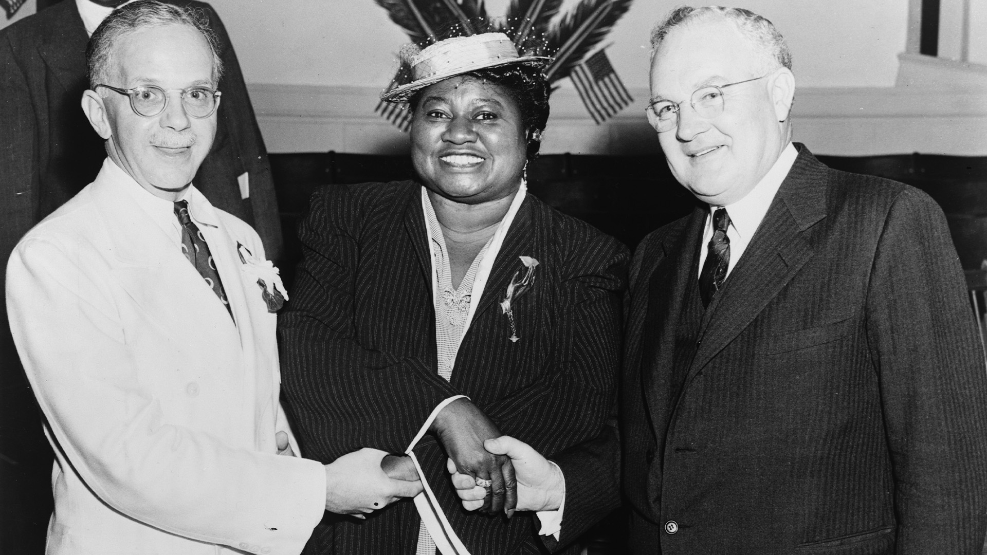 Walter F. White, standing to the left, shakes hands with NAACP leaders Hattie McDaniel, standing in the center, and Arthur Spingarn on the right.